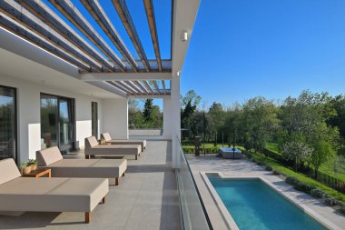 Güneş pansiyonlu modern lüks teras ve canlı yeşil manzaraya bakan ahşap pergola. Rahatlamak ve açık havada yaşamak için mükemmel. Gösterişli tasarım, cam korkuluklar ve doğal ışık..