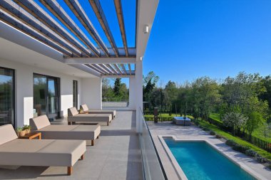 Güneş pansiyonlu modern lüks teras ve canlı yeşil manzaraya bakan ahşap pergola. Rahatlamak ve açık havada yaşamak için mükemmel. Gösterişli tasarım, cam korkuluklar ve doğal ışık..