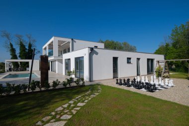 Güneşli bir günde havuzu, terası ve minimalist mimarisi olan modern lüks villa. Temiz hatlar, geniş pencereler ve açık yaşam alanları modern ev ortamları oluşturur..