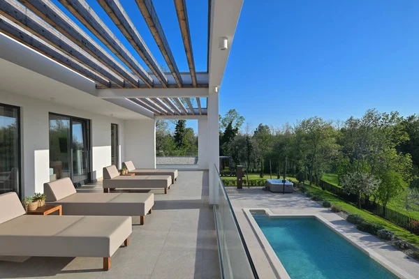 Güneş pansiyonlu modern lüks teras ve canlı yeşil manzaraya bakan ahşap pergola. Rahatlamak ve açık havada yaşamak için mükemmel. Gösterişli tasarım, cam korkuluklar ve doğal ışık..