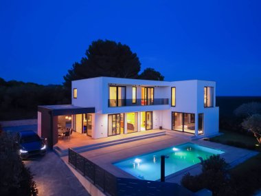 Alacakaranlıkta parlak bir yüzme havuzu olan modern lüks bir villa. Çağdaş mimari, şık tasarım ve davetkar iç ışıklar lüks bir ortam için ideal, sakin ve zarif bir akşam ortamı yaratır.