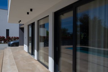 Yüzme havuzlu modern lüks villa ve mavi gökyüzünün altında temiz minimalist mimari. Geniş pencereler, teraslar ve zarif açık hava yaşam alanlarının bulunduğu çağdaş yerleşim alanı..