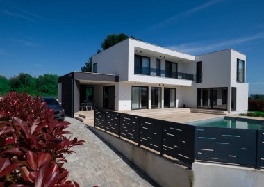 Yüzme havuzlu modern lüks villa ve mavi gökyüzünün altında temiz minimalist mimari. Geniş pencereler, teraslar ve zarif açık hava yaşam alanlarının bulunduğu çağdaş yerleşim alanı..