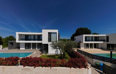 İki çarpıcı modern lüks villanın havadan görünüşü özel yüzme havuzları, zarif mimarisi ve yemyeşil peyzaj, güzel doğal bir zemine karşı kurulmuş..