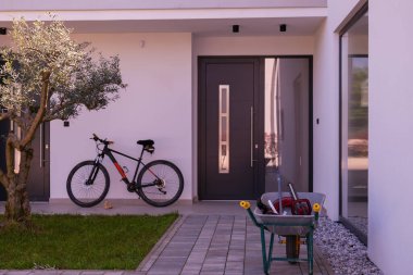 Minimalist mimarisi, ön kapısı, bisikleti ve peyzaj bahçesiyle modern yerleşim yeri girişi. Çağdaş ev dış görünüş temiz tasarım, günlük yaşam tarzı ve açık hava yaşam.
