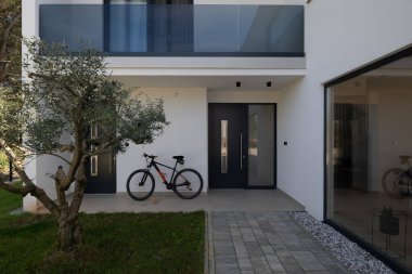 Minimalist mimarisi, ön kapısı, bisikleti ve peyzaj bahçesiyle modern yerleşim yeri girişi. Çağdaş ev dış görünüş temiz tasarım, günlük yaşam tarzı ve açık hava yaşam.