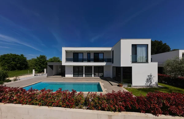 Yüzme havuzlu modern lüks villa ve mavi gökyüzünün altında temiz minimalist mimari. Geniş pencereler, teraslar ve zarif açık hava yaşam alanlarının bulunduğu çağdaş yerleşim alanı..