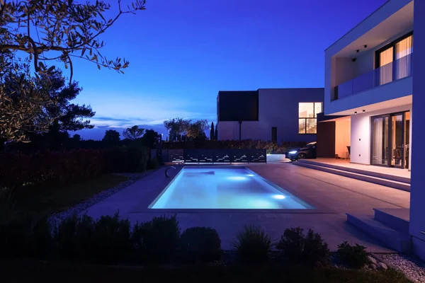 Alacakaranlıkta parlak bir yüzme havuzu olan modern lüks bir villa. Çağdaş mimari, şık tasarım ve davetkar iç ışıklar lüks bir ortam için ideal, sakin ve zarif bir akşam ortamı yaratır.