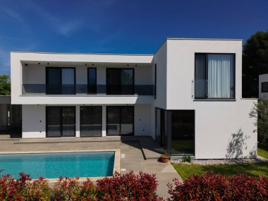Yüzme havuzlu modern lüks villa ve mavi gökyüzünün altında temiz minimalist mimari. Geniş pencereler, teraslar ve zarif açık hava yaşam alanlarının bulunduğu çağdaş yerleşim alanı..