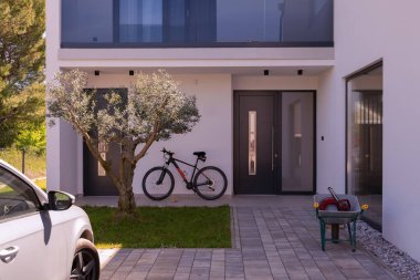 Minimalist mimarisi, ön kapısı, bisikleti ve peyzaj bahçesiyle modern yerleşim yeri girişi. Çağdaş ev dış görünüş temiz tasarım, günlük yaşam tarzı ve açık hava yaşam.