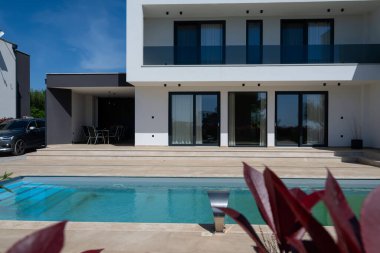 Yüzme havuzlu modern lüks villa ve mavi gökyüzünün altında temiz minimalist mimari. Geniş pencereler, teraslar ve zarif açık hava yaşam alanlarının bulunduğu çağdaş yerleşim alanı..