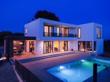 Alacakaranlıkta parlak bir yüzme havuzu olan modern lüks bir villa. Çağdaş mimari, şık tasarım ve davetkar iç ışıklar lüks bir ortam için ideal, sakin ve zarif bir akşam ortamı yaratır.