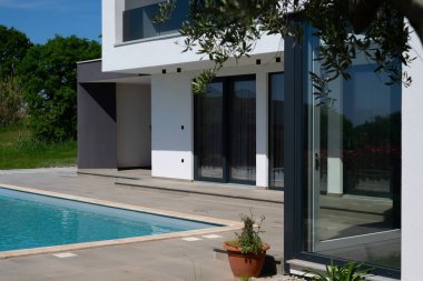 Yüzme havuzlu modern lüks villa ve mavi gökyüzünün altında temiz minimalist mimari. Geniş pencereler, teraslar ve zarif açık hava yaşam alanlarının bulunduğu çağdaş yerleşim alanı..