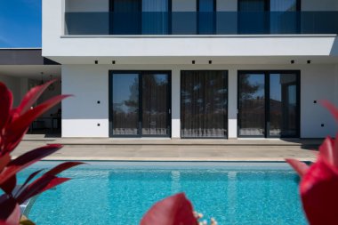 Yüzme havuzlu modern lüks villa ve mavi gökyüzünün altında temiz minimalist mimari. Geniş pencereler, teraslar ve zarif açık hava yaşam alanlarının bulunduğu çağdaş yerleşim alanı..