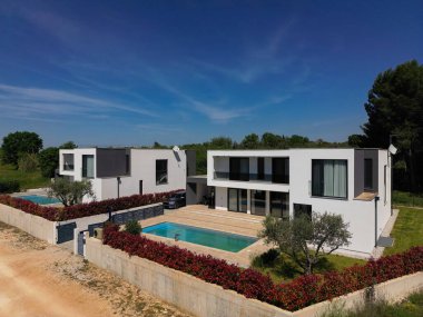 İki çarpıcı modern lüks villanın havadan görünüşü özel yüzme havuzları, zarif mimarisi ve yemyeşil peyzaj, güzel doğal bir zemine karşı kurulmuş..