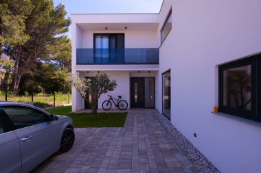 Minimalist mimarisi, ön kapısı, bisikleti ve peyzaj bahçesiyle modern yerleşim yeri girişi. Çağdaş ev dış görünüş temiz tasarım, günlük yaşam tarzı ve açık hava yaşam.