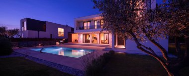 Alacakaranlıkta parlak bir yüzme havuzu olan modern lüks bir villa. Çağdaş mimari, şık tasarım ve davetkar iç ışıklar lüks bir ortam için ideal, sakin ve zarif bir akşam ortamı yaratır.