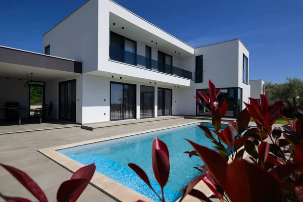 Yüzme havuzlu modern lüks villa ve mavi gökyüzünün altında temiz minimalist mimari. Geniş pencereler, teraslar ve zarif açık hava yaşam alanlarının bulunduğu çağdaş yerleşim alanı..