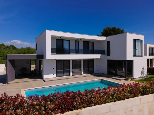 Yüzme havuzlu modern lüks villa ve mavi gökyüzünün altında temiz minimalist mimari. Geniş pencereler, teraslar ve zarif açık hava yaşam alanlarının bulunduğu çağdaş yerleşim alanı..