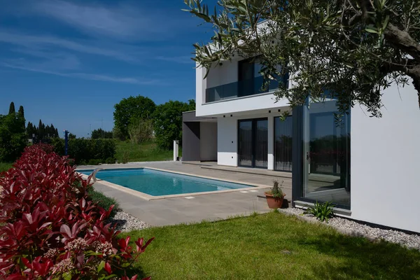 Yüzme havuzlu modern lüks villa ve mavi gökyüzünün altında temiz minimalist mimari. Geniş pencereler, teraslar ve zarif açık hava yaşam alanlarının bulunduğu çağdaş yerleşim alanı..