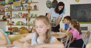 Bir sınıfta fen dersi sırasında bir grup meraklı ilkokul öğrencisine cam kavanozda teraryum bitkisini gösteren bayan öğretmen interaktif öğrenme ve keşfi teşvik ediyor. Sinema yavaşlığı