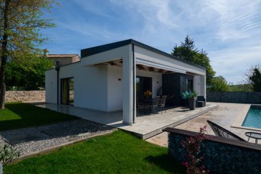 Yemek masası olan, yüzme havuzu ve çitlere bakan modern modüler bir evin terası. Dış mekanı olan çağdaş prefabrik ev mimarisi.