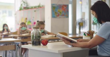 El hijyenini gösteren koruyucu bir maske takan kadın öğretmen ya da salgın ya da grip sezonunda sınıfta maske takan öğrencilere bir ders anlatıyor..