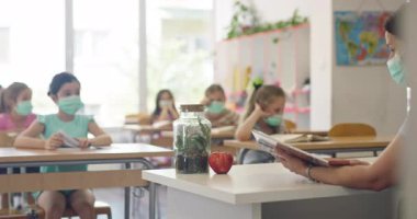 El hijyenini gösteren koruyucu bir maske takan kadın öğretmen ya da salgın ya da grip sezonunda sınıfta maske takan öğrencilere bir ders anlatıyor..