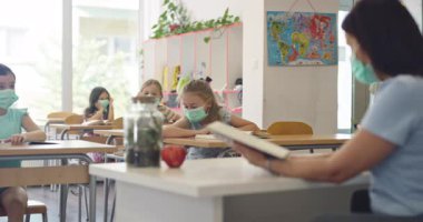 El hijyenini gösteren koruyucu bir maske takan kadın öğretmen ya da salgın ya da grip sezonunda sınıfta maske takan öğrencilere bir ders anlatıyor..