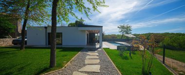 Dikdörtgen yüzme havuzu, ahşap güneş şezlongları ve mavi gökyüzüne karşı şemsiyeleri olan modern modüler evlerin arka bahçesi. Çağdaş prefabrik ev tasarımı.