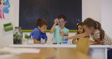 İlkokul öğrencilerinin sınıfta fen deneyi yapması, test tüpleri ve gözlük takması, STEM eğitimi, takım çalışması ve modern ilkokul laboratuvarında öğrenmesi. Sinematik ağır çekim