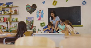 İlkokul öğrencilerine fen sınıfında deney tüpleri ve sıvılarla kimya deneyi yoluyla güvenlik gözlüğü takan bir öğrenciye rehberlik eden kadın öğretmen. Sinema yavaşlığı
