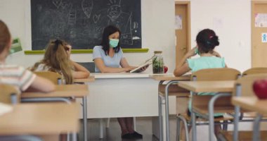 El hijyenini gösteren koruyucu bir maske takan kadın öğretmen ya da salgın ya da grip sezonunda sınıfta maske takan öğrencilere bir ders anlatıyor..