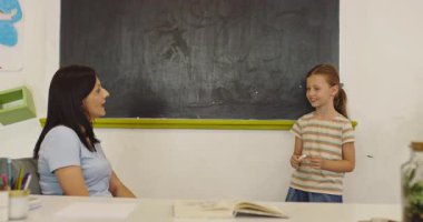 İlkokul öğrencileri sınıfta öğreniyor. Kız, öğretmenlerin yardımıyla tahtaya mektup yazıyor. Okuma yazma dersi, ilköğretim, modern okul içi..