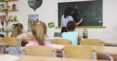 İlkokul öğrencileri sınıfta öğreniyor. Kız, öğretmenlerin yardımıyla tahtaya mektup yazıyor. Okuma yazma dersi, ilköğretim, modern okul içi..