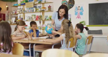 Öğretmen ve ilkokul öğrencileri sınıfta coğrafya öğreniyor, meraklı çocuklar birlikte dünya haritasını keşfediyorlar, sosyal bilimler ve çocuklar için küresel eğitim. Sinematik ağır çekim