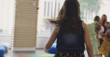 Modern bir anaokulu sınıfında ya da duyusal terapi odasında gülümseyen öğretmenlerinin etrafında koşup kovalamaca oynayan enerjik bir grup çocuk. Sinematik ağır çekim