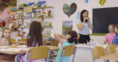 Sınıftaki heyecanlı ilkokul öğrencileri için balon ve çakmakla bilim deneyi yapan gülümseyen öğretmen, çocukların pop müzik beklentisiyle kulaklarını tıkarken,.