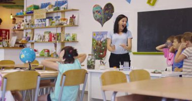 Sınıftaki heyecanlı ilkokul öğrencileri için balon ve çakmakla bilim deneyi yapan gülümseyen öğretmen, çocukların pop müzik beklentisiyle kulaklarını tıkarken,.