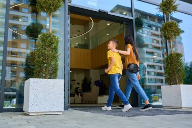 Bir erkek ve bir kız büyük cam kapıları olan modern bir binaya girerler. Arka planda şehrin ufuk çizgisi var ve mutlu ve meşgul görünüyorlar. Güneşli bir gün..
