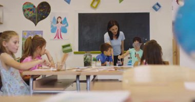 İlkokul öğrencilerine fen sınıfında deney tüpleri ve sıvılarla kimya deneyi yoluyla güvenlik gözlüğü takan bir öğrenciye rehberlik eden kadın öğretmen. Sinema yavaşlığı