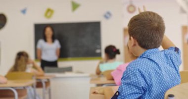 İlkokul öğrencileri sınıfta öğreniyor. Kız, öğretmenlerin yardımıyla tahtaya mektup yazıyor. Okuma yazma dersi, ilköğretim, modern okul içi..