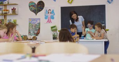 İlkokul öğrencilerine fen sınıfında deney tüpleri ve sıvılarla kimya deneyi yoluyla güvenlik gözlüğü takan bir öğrenciye rehberlik eden kadın öğretmen. Sinema yavaşlığı