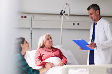 Bir doktor, ailesi parlak bir hastane odasında yanında otururken bir hastaya tedavi detaylarını anlatıyor. Atmosfer sıcak ve destekleyici, açık iletişimi teşvik ediyor..