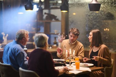 Dört kişi bir restoranda bir masada oturup Ramazan boyunca iftarın tadını çıkarıyor. Arka planda mumlar titreşirken yemek ve sohbet paylaşıyorlar..