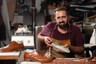 Meşgul bir atölyede deri önlük giyen, kahverengi deri ayakkabı giyen yetenekli bir ayakkabıcı. Aletler, bir ölçüm cetveli ve deri kırıntıları zanaat ve klasik zanaat sahnesi yaratır..