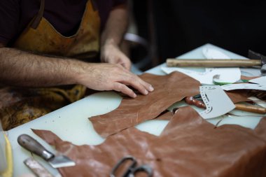 Yetenekli bir zanaatkar, el yapımı mallar yapmak için bıçaklar, keskiler ve desenler kullanarak deri parçalar üzerinde yoğunlaşır. Sahne, geleneksel işçilik, doku ve dokunsal kaliteyi vurguluyor