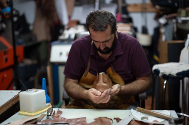 Bir zanaatkar, aletler ve kırıntılarla çevrili, geleneksel deri işçiliğine ve zanaat sanatına adanmış kahverengi bir deri ayakkabıyı hareketli bir atölyede şekillendirmeye odaklanır..