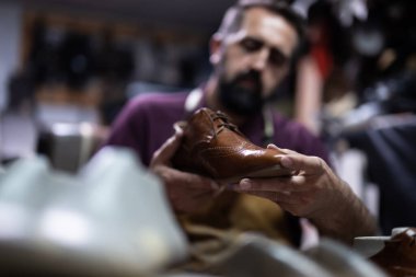 Yetenekli bir zanaatkar, yoğun bir atölyede kahverengi deri bir ayakkabıyı inceliyor, titizlik, işçilik ve geleneksel ayakkabı yapımındaki detaylara dikkat çekiyor..