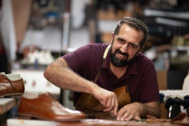 Dost canlısı bir zanaatkar deri atölyesinde çalışıyor, kahverengi bir çift ayakkabıyı şekillendirip parlatıyor. Sahne odaklanma, yetenek ve geleneksel ayakkabı yapma sanatını ön plana çıkarıyor.